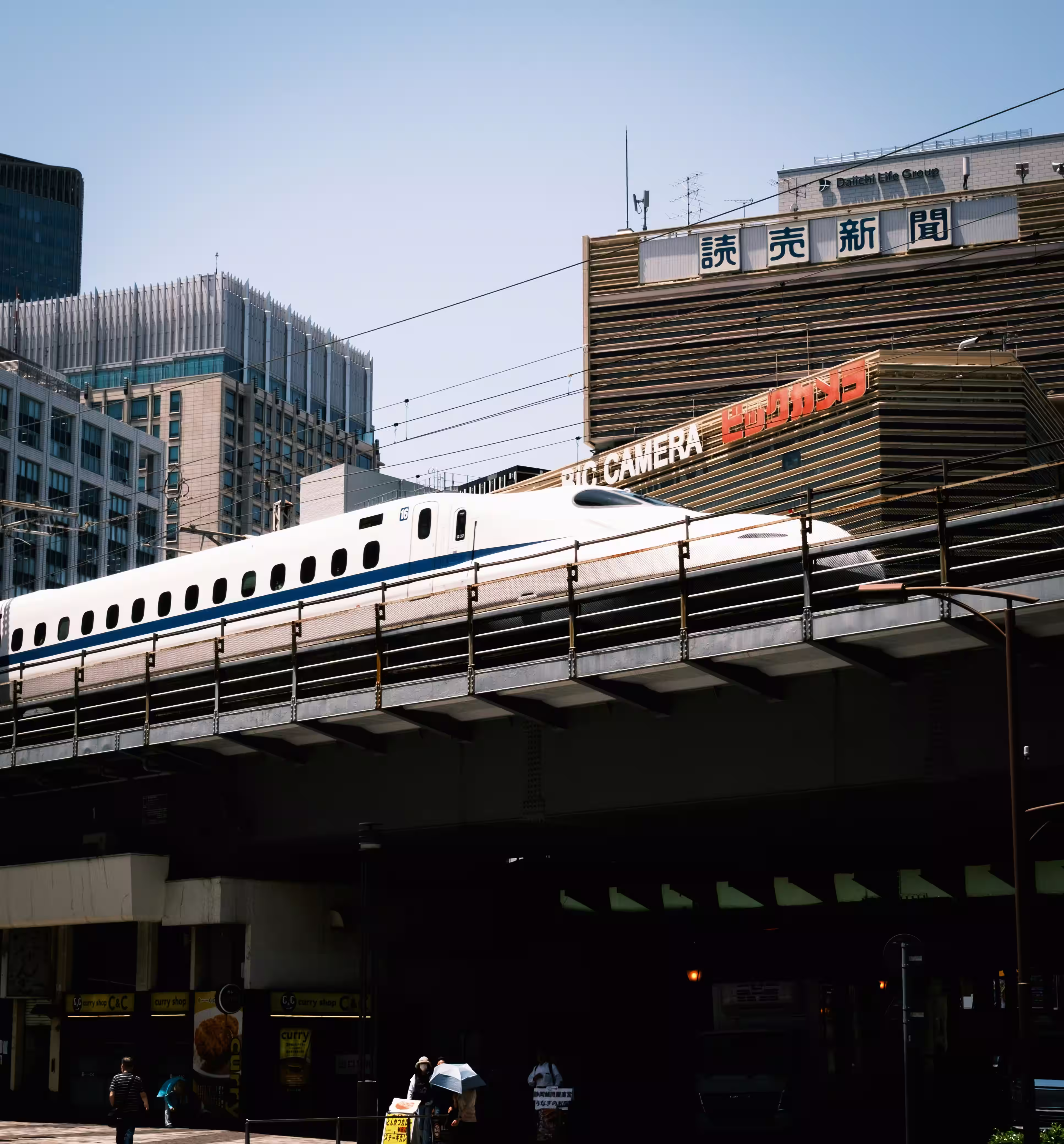 Shinkansen blanco y azul sobre vías elevadas entre edificios de una ciudad japonesa.
